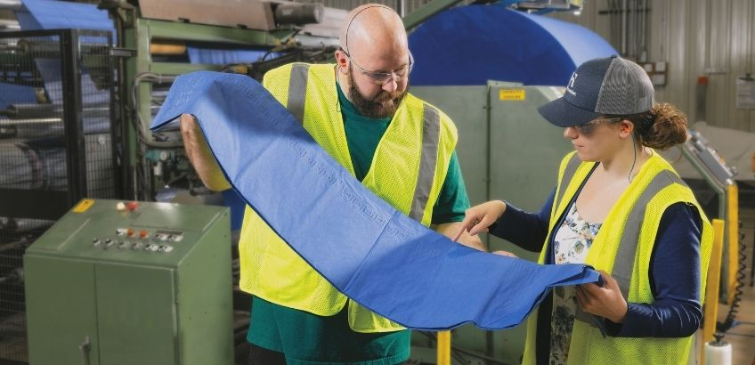 Two people reviewing quality of tablecover next to machine in facility