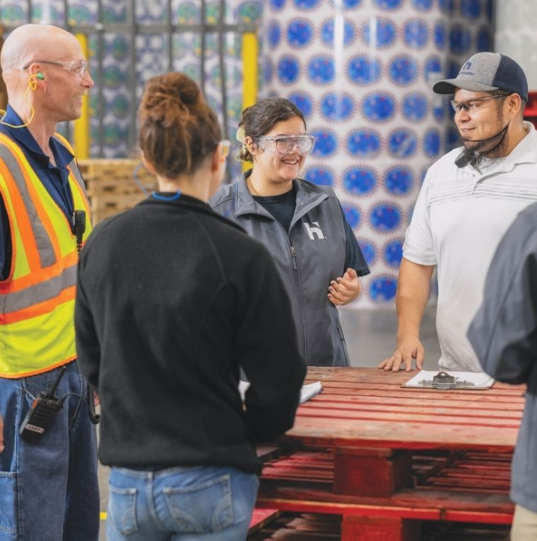 Manufacturing employees standing around pallet talking pre-shift